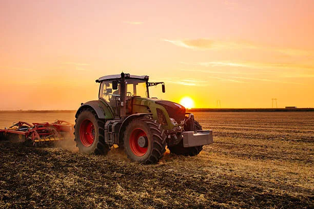 Un tracteur dans un champ au coucher du soleil protege par un GPS pour tracteur.