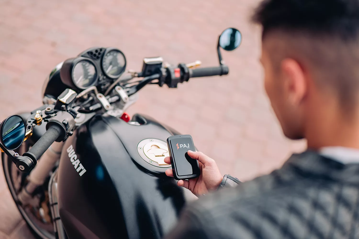 Un homme sur une moto avec le traceur GPS ALLROUND Finder 4G de PAj en main.