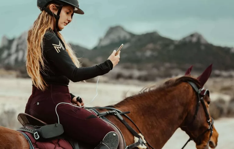 Une femme avec son smartphone en main sur un cheval