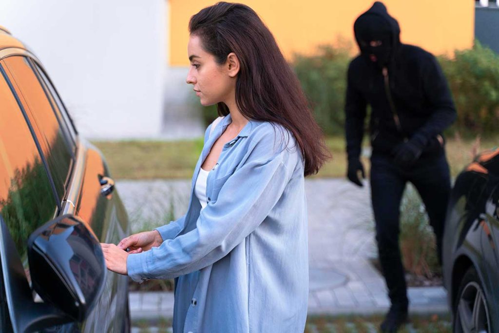 Une femme devant sa voiture avec un bandit derrière elle.