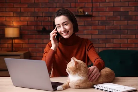 Une femme au téléphone regardant un ordinateur portable, un chat à ses côtés